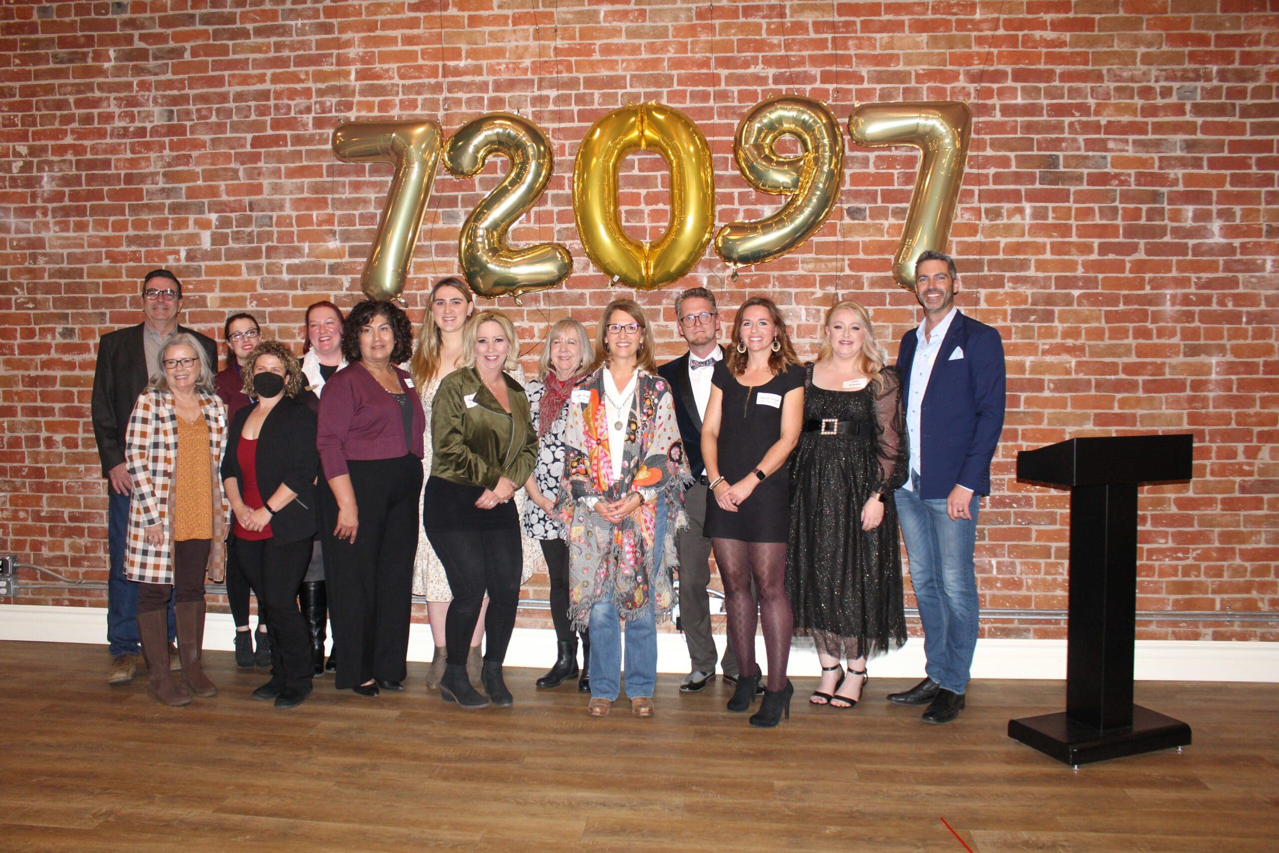 A group of people standing in front of a brick wall with balloons.
